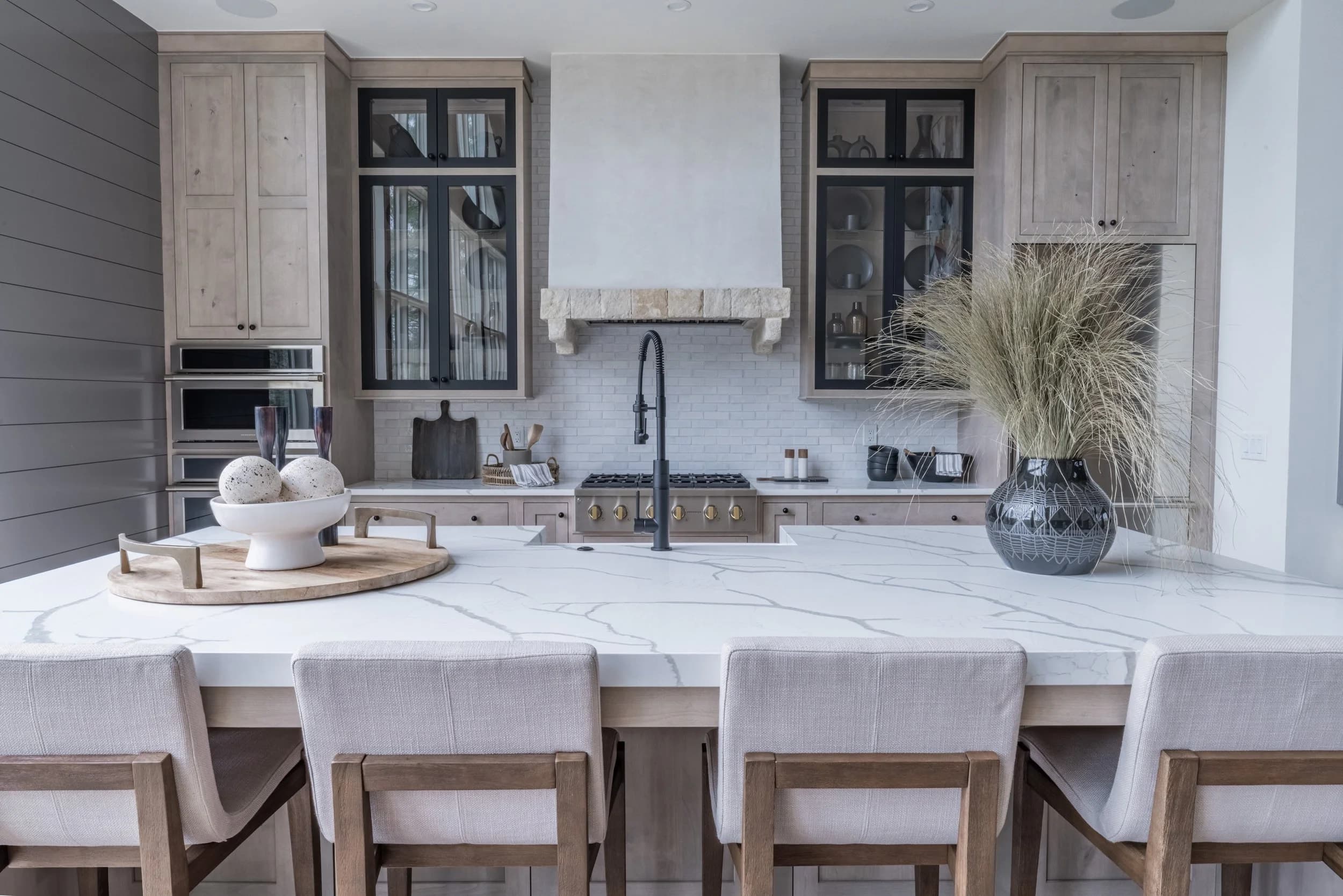 Light wood kitchen with a marble island, stone hood, and room for several seats.
