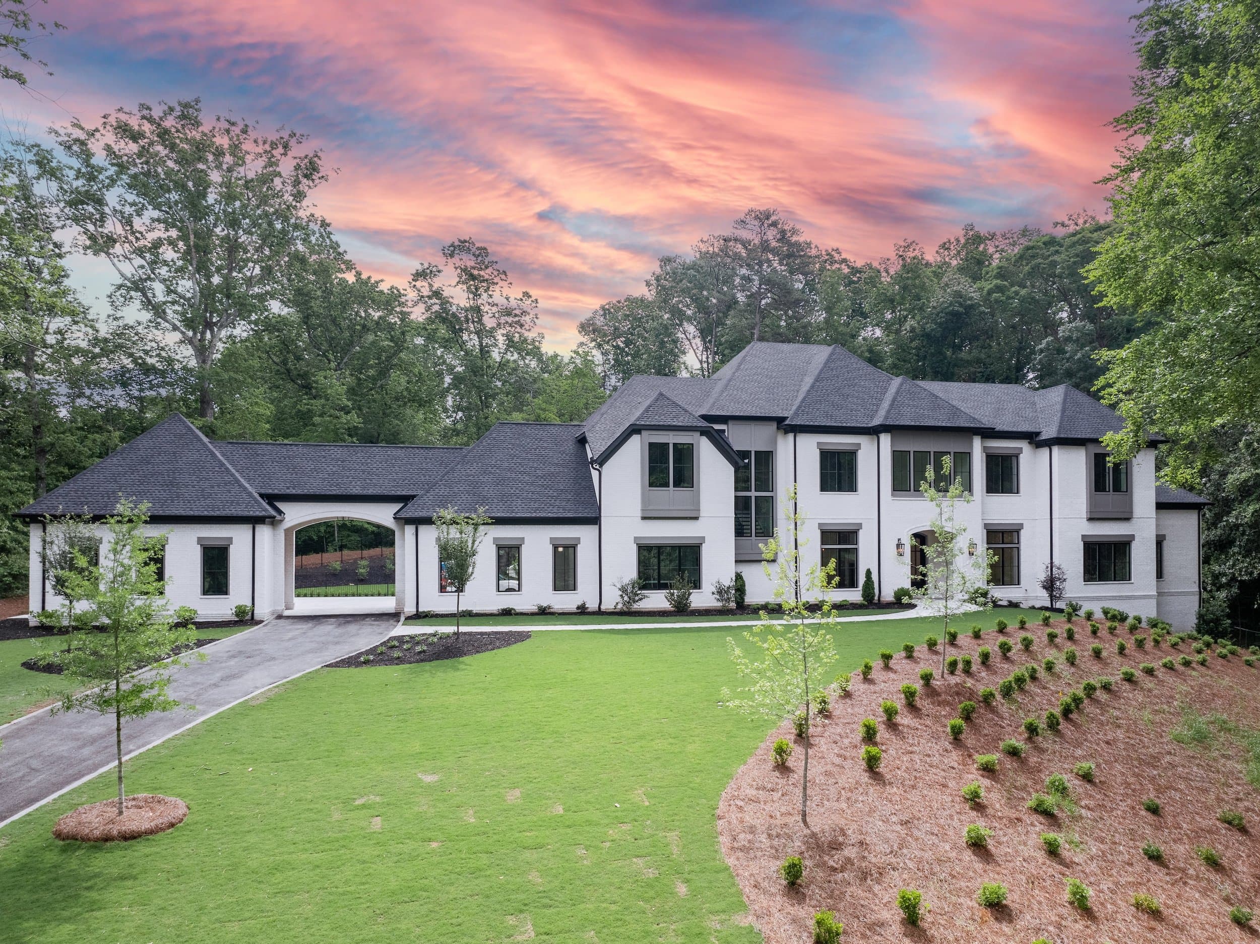 White custom home with a porte-cochère on a wooded lot at sunset.