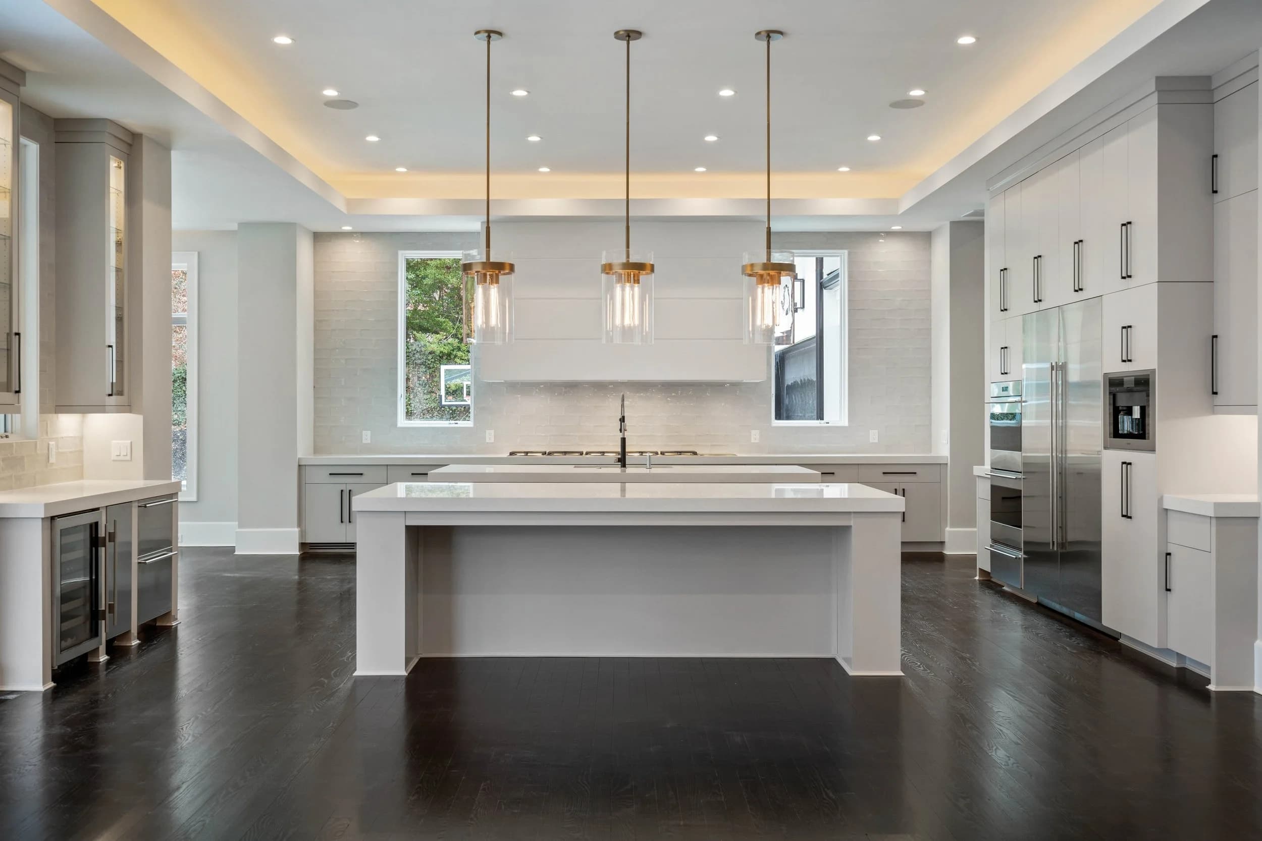Light gray kitchen with windows on either side of the range, a waterfall island, and a wine fridge.