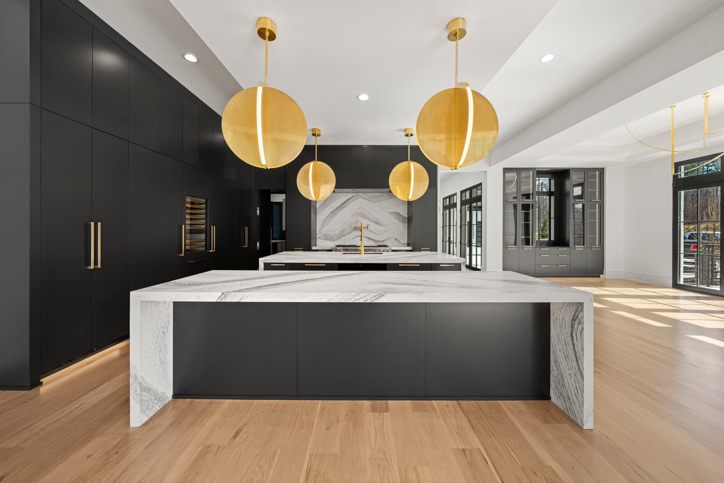 Black kitchen with a marble waterfall island, gold pendants, and brass hardware.
